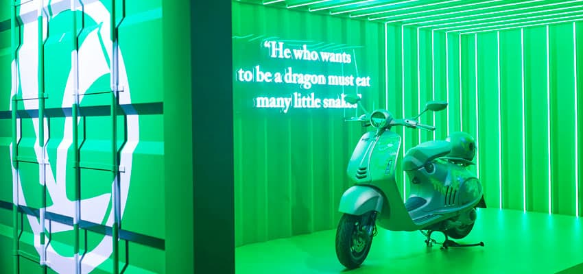 Imagen con color verde de una moto señoritera automática vespa en un contenedor para exhibirla