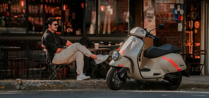 Hombre sentado en espacio público con su moto mostrando la mejor scooter automática en Colombia con Vespa Colombia
